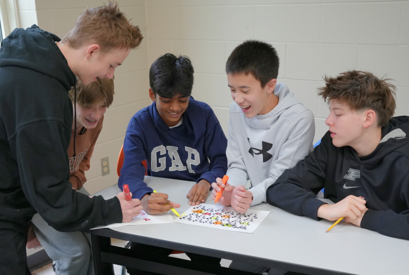 students smile and look at a sheet of paper on a desk as they complete an in-class activity